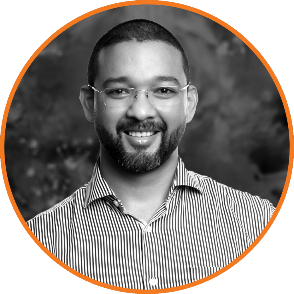 Smiling professional man named Delano with beard and glasses in a striped shirt, looking confidently at the camera.