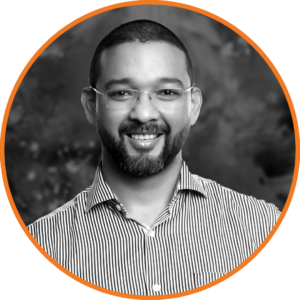 Smiling professional man named Delano with beard and glasses in a striped shirt, looking confidently at the camera.